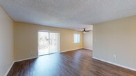 This single-floor residence offers a practical and well-organized layout across its living spaces. The main living area is generously proportioned, featuring rich hardwood-style flooring, warm neutral-toned walls, and a textured ceiling throughout. A ceiling fan provides added comfort, while a large sliding glass door with vertical blinds floods the space with natural light and provides direct access to the outdoors. An additional window further enhances the bright, open atmosphere of the living area.

The galley-style kitchen is equipped with warm honey-toned cabinetry, granite-look countertops, and a full suite of black appliances including a refrigerator, electric range with oven, and dishwasher. A stainless steel sink is positioned beneath a window, and ample upper and lower cabinet storage ensures a functional cooking environment. Hardwood-style flooring continues seamlessly into the kitchen.

The bedrooms feature plush wall-to-wall carpeting and neutral paint, offering a comfortable and quiet retreat. Each room benefits from natural light through windows dressed with vertical blinds. The bathroom is clean and well-appointed, featuring a full tub-shower combination, a dark-framed vanity mirror, white countertop, and wood-style flooring, presenting a tidy and functional space.