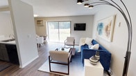 This single-floor residence offers a thoughtfully designed layout that balances comfort and functionality across its key living spaces. The living room serves as the heart of the unit, featuring wood-style flooring, a modern chandelier, and a large sliding glass door that fills the space with natural light and provides direct views of lush greenery. A dedicated dining area sits adjacent, accommodating a round table and seating. The kitchen is well-equipped, showcasing two-tone cabinetry with white upper cabinets and gray lower cabinets, white quartz countertops, a classic subway tile backsplash, and black appliances including a refrigerator, range, and microwave. A peninsula with a stainless steel sink adds workspace and separation from the dining area. The primary bedroom offers carpeted flooring and a large window with outdoor views, while a second room functions flexibly as a bedroom or home office, also carpeted and naturally lit. Two bathrooms serve the unit — one with a vanity and mirrored medicine cabinet, the other with a tub-shower combination. A dedicated laundry room houses a full-size washer and dryer alongside a water heater, completing this practical and move-in ready space.