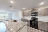 Located at 1928 Waycrest Dr SW in Atlanta, Georgia, this single-floor, two-bedroom, two-bathroom home offers a thoughtfully designed open layout with modern finishes throughout. The combined kitchen and living area serves as the heart of the home, featuring a central island with a granite countertop and built-in sink, taupe cabinetry, and black appliances including a gas range, microwave, and refrigerator. Light wood-style flooring flows seamlessly throughout the space, complementing the clean white walls and recessed lighting.

The living area benefits from a large window that invites natural light and offers views of surrounding greenery, with a ceiling fan adding comfort overhead. Both bedrooms are well-proportioned, each equipped with ceiling fans and generous windows that frame outdoor views. The primary bedroom provides a comfortable retreat with dedicated closet space. Four closets in total offer ample storage across the home.

Both bathrooms mirror the home's consistent design aesthetic, featuring granite-topped vanities with dark cabinetry and light wood-style flooring. One bathroom includes a full tub-shower combination. Additional conveniences include a dedicated laundry area and a utility room, rounding out this efficiently designed and move-in-ready home.
