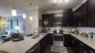 This single-floor residence showcases a thoughtfully designed interior with a focus on modern aesthetics and functional living. The kitchen serves as a standout feature, boasting rich, dark espresso-toned cabinetry that extends to the upper walls, providing generous storage space. Speckled granite countertops run throughout, offering ample prep space and a clean, polished finish. Stainless steel appliances, including a range, built-in microwave, and dishwasher, lend a professional and contemporary feel to the cooking space. A double-basin undermount sink is positioned along the extended counter peninsula, making it both practical and central to the kitchen layout. Elegant pendant lighting hangs above the peninsula, adding warmth and a decorative touch, while recessed track lighting illuminates the main cooking area. Crown molding details along the ceiling add a refined architectural element that elevates the overall aesthetic. Dark hardwood-style flooring grounds the space and complements the cabinetry beautifully. The open layout of the kitchen allows for a natural flow into adjacent living areas, making it well-suited for both everyday living and entertaining.
