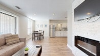 Located at 10105 Wornall Rd in Kansas City, MO, this single-floor unit combines modern design with functional living. The open-concept layout connects the living room, dining area, and kitchen, creating a seamless flow throughout the main living space. Light wood-tone flooring extends across the entire unit, complementing the neutral color palette of warm grays and crisp whites.

The living room is anchored by a striking floor-to-ceiling stacked stone fireplace with a sleek, modern insert and a wall-mounted television above. Natural light enters through multiple windows fitted with blinds. The adjacent dining area comfortably accommodates a four-person table and benefits from its own window.

The kitchen is well-appointed with white shaker-style cabinetry, stainless steel appliances including a full-size refrigerator, range, and microwave, as well as a mosaic tile backsplash that adds a contemporary detail.

Both bedrooms feature warm-toned walls, recessed lighting, and light wood flooring. One bedroom includes a walk-in closet, offering practical storage. The bathroom is finished with large-format marble-look wall tile surrounding a soaking tub and shower combination, a decorative tile accent border, and built-in niche shelving for added convenience.
