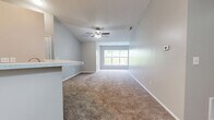 Located at 707 River Dr in Lawrenceburg, Indiana, this single-floor, 2-bedroom residence offers a practical and comfortable layout across a well-organized floor plan. The open-concept living, dining, and kitchen area forms the heart of the home, with plush carpeting flowing through the living and dining spaces. A ceiling fan overhead and a wide window at the far end of the living room invite natural light and views of the surrounding greenery. The kitchen is defined by white cabinetry, wood-look flooring, recessed lighting, and black appliances including a range and refrigerator. A peninsula with a light-colored countertop provides seating and serves as a natural divider between the kitchen and living area. The primary bedroom is generously sized, featuring carpet, neutral gray walls, and direct access to a private en-suite bathroom with a vanity, mirror, and shower. The second bedroom also offers carpeted floors, a walk-in closet with built-in shelving, and a window with outdoor views. A hallway connects the bedrooms to the rest of the home, with two closets providing additional storage. The overall color palette of soft grays and whites lends the space a clean, neutral ambiance throughout.