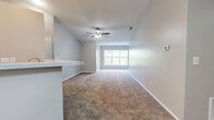 Located at 707 River Dr in Lawrenceburg, Indiana, this single-floor, 2-bedroom residence offers a practical and comfortable layout across a well-organized floor plan. The open-concept living, dining, and kitchen area forms the heart of the home, with plush carpeting flowing through the living and dining spaces. A ceiling fan overhead and a wide window at the far end of the living room invite natural light and views of the surrounding greenery. The kitchen is defined by white cabinetry, wood-look flooring, recessed lighting, and black appliances including a range and refrigerator. A peninsula with a light-colored countertop provides seating and serves as a natural divider between the kitchen and living area. The primary bedroom is generously sized, featuring carpet, neutral gray walls, and direct access to a private en-suite bathroom with a vanity, mirror, and shower. The second bedroom also offers carpeted floors, a walk-in closet with built-in shelving, and a window with outdoor views. A hallway connects the bedrooms to the rest of the home, with two closets providing additional storage. The overall color palette of soft grays and whites lends the space a clean, neutral ambiance throughout.