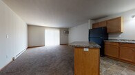 This single-floor unit offers a practical, open-concept layout where the kitchen flows directly into the spacious living area. The kitchen is well-equipped with warm honey-toned cabinetry, dark granite-style countertops, and a full suite of black appliances, including a refrigerator, range, dishwasher, and microwave. A peninsula with matching countertop and built-in electrical outlets serves as a natural divider between the kitchen and living space, providing additional prep or seating area. Stone-look tile flooring runs throughout the kitchen, adding durability in high-traffic areas.

The living area is generously sized, carpeted in neutral tones, and features a large sliding glass door dressed with vertical blinds that allows natural light to fill the space. A wall-mounted air conditioning unit provides supplemental climate control, complemented by baseboard heating found throughout the unit.

The bedroom is comfortably proportioned, carpeted, and includes a window with blinds and both a wall AC unit and baseboard heater. The bathroom features matching cabinetry with granite-style counters and tile flooring. A dedicated laundry area houses a full-size washer and dryer, adding everyday convenience.