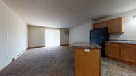 This single-floor unit offers a practical, open-concept layout where the kitchen flows directly into the spacious living area. The kitchen is well-equipped with warm honey-toned cabinetry, dark granite-style countertops, and a full suite of black appliances, including a refrigerator, range, dishwasher, and microwave. A peninsula with matching countertop and built-in electrical outlets serves as a natural divider between the kitchen and living space, providing additional prep or seating area. Stone-look tile flooring runs throughout the kitchen, adding durability in high-traffic areas.

The living area is generously sized, carpeted in neutral tones, and features a large sliding glass door dressed with vertical blinds that allows natural light to fill the space. A wall-mounted air conditioning unit provides supplemental climate control, complemented by baseboard heating found throughout the unit.

The bedroom is comfortably proportioned, carpeted, and includes a window with blinds and both a wall AC unit and baseboard heater. The bathroom features matching cabinetry with granite-style counters and tile flooring. A dedicated laundry area houses a full-size washer and dryer, adding everyday convenience.