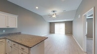 This single-floor home offers a thoughtfully designed layout with a neutral gray color palette and modern finishes throughout. The open-concept living area is a standout feature, showcasing soaring vaulted ceilings with a ceiling fan, light-toned wood-look tile flooring, and a sliding glass door fitted with vertical blinds that fills the space with natural light. The kitchen is well-equipped with crisp white cabinetry, granite countertops, a center island with additional seating, and a full suite of stainless steel appliances including a refrigerator, range, microwave, and dishwasher. The kitchen flows seamlessly into the living area, creating an ideal open-plan environment. The primary bedroom features a distinctive tray ceiling with a ceiling fan, plush carpeting, and direct access to a private en-suite bathroom. The en-suite is outfitted with granite countertops, white cabinetry, and a glass-enclosed walk-in shower with tile flooring. Additional bedrooms are carpeted and include windows with blinds for natural light, with at least one room featuring a built-in closet with paneled double doors. Throughout the home, consistent gray tones, clean white trim, and recessed lighting create a cohesive and contemporary ambiance.