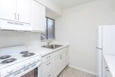 This single-floor unit in Royal Oak, Michigan, offers a well-organized layout designed for comfortable everyday living. The kitchen is efficiently arranged with white cabinetry, white laminate countertops, and a stainless steel sink positioned beneath a window fitted with horizontal blinds, allowing natural light to brighten the workspace. A white electric coil range with an overhead exhaust hood and a full-size refrigerator complete the kitchen's appliances, providing all essential cooking amenities.

The living area features neutral-toned carpet flooring and is illuminated by a central pendant light fixture. A pass-through opening connects this space to the kitchen, enhancing the sense of openness. A sliding glass door leads directly to an outdoor green area, bringing in abundant natural light and providing easy exterior access.

The bedroom is carpeted and features a window that allows natural light to enter, keeping the space bright and airy.

The bathroom is finished with small-format mosaic tile flooring and includes a sliding glass-door shower enclosure with a grab bar, a toilet, and a white vanity with an integrated sink and a large mirror above. The clean, neutral palette throughout the unit creates a cohesive and welcoming atmosphere.
