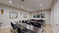 Located at 3500 Granada Avenue in Santa Clara, California, this 480-square-foot meeting and training room is thoughtfully designed to support professional gatherings, presentations, and educational sessions. The single-floor space features a classic classroom-style layout with rows of dark rectangular tables paired with ergonomic black rolling chairs, comfortably accommodating a sizeable group of attendees. A large flat-screen display is mounted at the front of the room, serving as the primary visual aid for presentations, while a full-size whiteboard on the adjacent wall provides a flexible surface for note-taking and collaborative work. The room is finished with light wood-toned flooring that lends a clean, contemporary feel to the space. Recessed ceiling lighting ensures even, well-distributed illumination throughout. The neutral beige walls are accented with decorative framed artwork in abstract and geometric styles, as well as subtle wall-mounted wooden décor elements that add warmth and visual interest. The layout is open and practical, with ample circulation space around the perimeter. This versatile meeting space is well-suited for corporate training sessions, seminars, workshops, and team meetings in the heart of Silicon Valley.