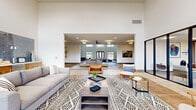 This expansive single-floor amenity center offers a thoughtfully designed collection of spaces that blend modern aesthetics with functional comfort. The centerpiece is a grand lounge area distinguished by soaring double-height ceilings, a coffered tray ceiling with recessed lighting, and an abundance of natural light streaming through large clerestory windows and glass doors. The open layout flows seamlessly between multiple seating arrangements, anchored by patterned area rugs and a mix of contemporary and mid-century modern furnishings.

A dedicated dining room provides a formal gathering space, centered around a large rectangular conference-style table with upholstered chairs and elegant pendant lighting overhead. Adjacent to this is a well-appointed kitchen featuring warm wood cabinetry, granite countertops, and durable tile flooring. The business office offers two workstations with mounted monitors, providing a quiet and productive environment.

A standout feature is the full-service salon, finished with earthy stone-tile accent walls, illuminated vanity mirrors, professional styling chairs, and a shampoo station — delivering a spa-like atmosphere. The exercise room is generously sized, equipped with cardio machines, free weights, and exercise balls, complemented by ceiling fans and large windows. Wide, warmly lit hallways connect all areas, finished with wood-look tile flooring and curated artwork throughout.