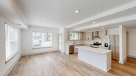 Located at 15120 Idlewild Road in Matthews, NC, this well-appointed 3-bedroom, 2-bathroom residence offers a thoughtfully designed single-level layout. The open-concept kitchen and living area serves as the heart of the home, featuring light gray shaker cabinetry, white quartz countertops, a subway tile backsplash, stainless steel appliances, a dedicated range hood, and a large center island — ideal for both cooking and casual dining. Wood-look luxury flooring flows throughout the main living areas, complemented by recessed lighting and an abundance of natural light from multiple windows overlooking the surrounding greenery. The spacious primary bedroom includes a ceiling fan and plush carpeting, while its en-suite bathroom impresses with a dual-sink vanity, sleek black hardware, a framed mirror, and a glass-enclosed tile shower. The generously sized walk-in closet offers wire shelving along multiple walls for ample storage. Two additional bedrooms share a second full bathroom. A dedicated hallway connects the rooms efficiently. The building itself presents a modern exterior with a mix of dark paneling and brick, set within a well-maintained community in Matthews, NC.