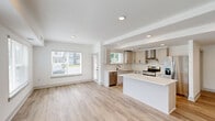 Located at 15120 Idlewild Road in Matthews, NC, this well-appointed 3-bedroom, 2-bathroom residence offers a thoughtfully designed single-level layout. The open-concept kitchen and living area serves as the heart of the home, featuring light gray shaker cabinetry, white quartz countertops, a subway tile backsplash, stainless steel appliances, a dedicated range hood, and a large center island — ideal for both cooking and casual dining. Wood-look luxury flooring flows throughout the main living areas, complemented by recessed lighting and an abundance of natural light from multiple windows overlooking the surrounding greenery. The spacious primary bedroom includes a ceiling fan and plush carpeting, while its en-suite bathroom impresses with a dual-sink vanity, sleek black hardware, a framed mirror, and a glass-enclosed tile shower. The generously sized walk-in closet offers wire shelving along multiple walls for ample storage. Two additional bedrooms share a second full bathroom. A dedicated hallway connects the rooms efficiently. The building itself presents a modern exterior with a mix of dark paneling and brick, set within a well-maintained community in Matthews, NC.