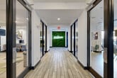 Located at 101 Church Ave in College Station, TX, this single-floor amenity facility offers an expansive and thoughtfully designed space built to serve a variety of lifestyle and productivity needs. A striking central hallway sets the tone upon entry, featuring wood-look tile flooring, glass-partitioned rooms along each side, and an eye-catching living green wall adorned with a glowing "#LiveDomain" neon sign that anchors the corridor with bold, modern character.

The facility's fitness center is a standout feature, occupying a generous footprint and outfitted with an extensive array of strength machines, cable systems, free weights, kettlebells, and cardio equipment. Durable rubber flooring, bright overhead lighting, and ceiling fans contribute to a functional, well-equipped workout environment. An adjacent flex room with hardwood-style flooring provides space for stretching, functional training, or group exercise.

The lounge and kitchen area features a large white quartz island with bar seating, stainless steel appliances, a Starbucks coffee station, a wall-mounted TV, and geometric accent tile — all illuminated by warm woven pendant lights. A dedicated business center offers workstations with desktop computers, modern seating, and curated wall art. Collaborative study rooms provide flexible seating, whiteboards, and natural window light, while casual social nooks with bistro tables offer informal gathering spots throughout.