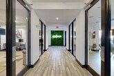 Located at 101 Church Ave in College Station, TX, this single-floor amenity facility offers an expansive and thoughtfully designed space built to serve a variety of lifestyle and productivity needs. A striking central hallway sets the tone upon entry, featuring wood-look tile flooring, glass-partitioned rooms along each side, and an eye-catching living green wall adorned with a glowing "#LiveDomain" neon sign that anchors the corridor with bold, modern character.

The facility's fitness center is a standout feature, occupying a generous footprint and outfitted with an extensive array of strength machines, cable systems, free weights, kettlebells, and cardio equipment. Durable rubber flooring, bright overhead lighting, and ceiling fans contribute to a functional, well-equipped workout environment. An adjacent flex room with hardwood-style flooring provides space for stretching, functional training, or group exercise.

The lounge and kitchen area features a large white quartz island with bar seating, stainless steel appliances, a Starbucks coffee station, a wall-mounted TV, and geometric accent tile — all illuminated by warm woven pendant lights. A dedicated business center offers workstations with desktop computers, modern seating, and curated wall art. Collaborative study rooms provide flexible seating, whiteboards, and natural window light, while casual social nooks with bistro tables offer informal gathering spots throughout.