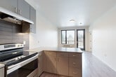Located at 636 W 6th St in Vancouver, WA, this modern one-bedroom, one-bathroom unit offers a thoughtfully designed layout across a single floor. The open-concept kitchen is a standout feature, showcasing sleek gray flat-front cabinetry extending to the ceiling, a textured tile backsplash, stone-look countertops, and a full suite of stainless steel appliances including a refrigerator, electric range, and dishwasher. A peninsula with additional cabinetry and counter space visually connects the kitchen to the dining and living areas, creating a cohesive, functional flow throughout. Light wood-look flooring runs continuously through the main living spaces, enhancing the clean, contemporary aesthetic. The living and dining area is brightened by large windows and a glass-paneled door that frames views of mature trees, inviting natural light deep into the unit. The bedroom is a calm, well-proportioned retreat with its own window overlooking the greenery outside and wood-look flooring underfoot. A closet provides dedicated storage. The bathroom features a full tub-shower combination with clean white surrounds and chrome fixtures. A bold navy entry door with modern hardware makes a striking first impression upon arrival.