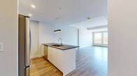 This thoughtfully designed 1-bedroom, 1-bathroom unit at 6450 Bayers Road in Halifax offers a clean, modern aesthetic throughout. The open-concept kitchen and living area form the heart of the home, anchored by a sleek kitchen island with a dark countertop, undermount sink, and contemporary pendant lighting. The kitchen is equipped with stainless steel appliances, white cabinetry extending to the ceiling, and a wood-toned tile backsplash that adds warmth to the otherwise crisp palette. Light hardwood-style flooring flows seamlessly throughout the unit, complementing the bright, neutral walls. The living area is generously proportioned, bathed in natural light from large windows offering outdoor views of the surrounding neighbourhood. The bedroom is a comfortable size, featuring a built-in closet with shelving, a baseboard heater, and direct access to the private balcony through a sliding glass door. A wall-mounted mini-split unit provides additional climate control. The full bathroom is cleanly finished with a tub-shower combination, white cabinetry, and dark countertops. A utility room rounds out the layout, adding practical storage and functionality to this well-appointed urban residence.