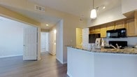 This 2-bedroom, 2-bathroom Chesapeake Platinum residence is a single-story layout designed with both functionality and style in mind. The open-concept kitchen serves as a central highlight, featuring warm honey-toned cabinetry, granite-look countertops, and a peninsula with a crisp white base that provides additional prep space and casual seating. A stylish pendant light hangs above the peninsula, complemented by track lighting that keeps the kitchen bright and inviting. Black appliances, including a refrigerator, add a contemporary contrast to the warm cabinetry tones.

The kitchen flows seamlessly into the living areas, with durable wood-style flooring extending throughout the main spaces, adding warmth and cohesion. A hallway connects the two bedrooms, each offering privacy with their own access to well-appointed bathrooms. The corridor features multiple doors, suggesting ample closet storage throughout the unit.

Neutral wall tones in soft beige create a versatile backdrop that complements various décor styles. Recessed lighting and HVAC vents integrated into the ceiling ensure year-round comfort. The overall ambiance is clean, modern, and move-in ready, making this a practical yet stylish living space.