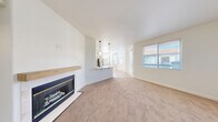 Located at 9625 W Russell Rd in Las Vegas, NV, this 2-bedroom, 2-bathroom residence offers a thoughtfully designed single-story layout with a clean, contemporary aesthetic throughout. The open-concept living area serves as the heart of the home, featuring plush carpeting, a sleek fireplace with a wood mantle and tile surround, and large windows that invite an abundance of natural light. The space flows seamlessly into a combined dining area and modern kitchen, which is outfitted with white shaker cabinetry, a subway tile backsplash, stainless steel appliances including a gas range and refrigerator, and a peninsula with a white quartz countertop — all set atop light wood-style flooring. A private balcony extends the living space outdoors. The spacious primary bedroom features carpeted floors, natural light from a generously sized window, and access to a walk-in closet with ample wire shelving. The second bedroom is equally bright and well-proportioned. Both bathrooms are finished with wood-look flooring, white cabinetry, and matte black fixtures, with one featuring a tub-shower combination. Additional conveniences include an in-unit laundry area and a hallway connecting the home's key spaces efficiently.