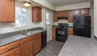 Located at 2495 Livernois Rd in Troy, Michigan, this multi-level residence spans three floors, offering a thoughtfully arranged layout designed for comfortable everyday living. The main level welcomes you with a spacious living area featuring rich hardwood-style flooring, a large picture window that draws in generous natural light and offers views of the surrounding greenery, and a staircase leading to the upper level. A coat closet is conveniently positioned near the front entry. The kitchen is well-equipped with warm medium-toned wood cabinetry, dark granite-style countertops, and a full suite of black appliances including a gas range, dishwasher, and refrigerator. A double sink beneath a window adds functionality and light. A compact half-bath with a wood vanity and wood-style flooring serves the main level. Upstairs, the carpeted bedrooms provide a quiet retreat, each painted in neutral tones and featuring windows for natural light. A full bathroom on this level includes a white vanity, tub-shower combination with tile surround, and a window for ventilation. The unfinished basement offers significant utility space with painted concrete floors and walls, exposed beam ceilings, a water heater, and electrical panel access, providing ample potential for storage or future finishing.