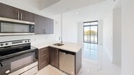 Located at 1 Curtiss Pkwy in Miami Springs, FL, this contemporary 2-bedroom, 4-bathroom residence offers a thoughtfully designed single-floor layout with modern finishes throughout. Large-format marble-look porcelain tile flooring flows seamlessly through every room, lending a clean and sophisticated aesthetic to the entire space.

The open-concept kitchen is a standout feature, equipped with stainless steel appliances — including a refrigerator, range, built-in microwave, and dishwasher — complemented by rich dark wood cabinetry and crisp quartz countertops with a peninsula that opens to the living area. Floor-to-ceiling windows and a glass-panel sliding door flood the living space with natural light and provide views of the surrounding greenery.

The generously sized primary bedroom offers ample room for comfortable living, while the second bedroom is bright and well-proportioned. The four bathrooms feature consistent marble-look tile finishes, with at least one bathroom showcasing a full soaking tub with a tiled surround and a vanity with stylish cabinetry. A dedicated in-unit laundry area houses a full-size washer and dryer with overhead shelving. The overall ambiance is light, airy, and modern — ideal for contemporary urban living in South Florida.