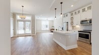 Located at 17014 Fairmount Way in Charlotte, NC, this two-story home combines clean, modern design with warm, inviting finishes throughout. The main level centers around a bright, open-concept living and dining area bathed in natural light from multiple large windows, all set over durable hardwood-style flooring. Crown molding adds a refined touch to the living spaces.

The kitchen is a true highlight, featuring floor-to-ceiling white cabinetry with glass-front upper panels and decorative X-detail accents, a large center island with a white quartz countertop and undermount sink, stainless steel appliances, and a tile backsplash. Pendant lighting with glass globe fixtures adds character overhead. A built-in wine cooler nestled within a custom niche near the entryway completes the main level's functional elegance.

The front entry welcomes with a transom-lit door and an open sightline into the living area. Upstairs, carpeted bedrooms offer comfortable retreats, each filled with natural light from generously sized windows. The upper-level hallway is carpeted and transitions smoothly between rooms. The bathroom features large-format tile flooring, a glass-enclosed shower with marble-style tile surround, a soaking tub, and white vanity cabinetry with oil-rubbed bronze fixtures throughout.
