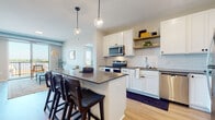 This well-appointed single-floor residence combines modern design with functional living. The open-concept kitchen serves as the heart of the home, showcasing white shaker cabinetry, a classic subway tile backsplash, dark quartz countertops, and a full suite of stainless steel appliances. A generously sized central island with bar seating and pendant globe lighting above makes it ideal for both meal preparation and casual dining. Warm light wood flooring extends throughout the main living areas, adding continuity and warmth.

The living room is bright and airy, benefiting from large sliding glass doors that open to a private balcony with outdoor views. A built-in desk nook with open shelving provides a dedicated workspace within the living area. The bedroom offers plush carpeting, a closet, and a sizable window that fills the room with natural light.

The primary bathroom features a dual-sink vanity with white cabinetry, dark hardware, and quartz countertops, paired with a tub-shower combination. A secondary bathroom mirrors the same refined aesthetic with a single vanity, quartz countertop, and matte black fixtures. Throughout the residence, neutral tones and clean lines create a cohesive, contemporary ambiance.