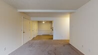 This single-floor residence at 3315 W Mount Hope Ave in Lansing, Michigan offers a straightforward, functional layout across several interconnected rooms. The living area is generously sized, featuring neutral-toned carpet underfoot, a textured ceiling, and exposed beam detailing that adds subtle architectural character. A wide opening connects the living space to an adjoining area, creating an open, flowing feel throughout. Vertical blinds on the windows allow natural light to filter in while maintaining privacy, and baseboard heating units run along the walls throughout the unit.

The kitchen is thoughtfully updated, featuring white cabinetry that extends to the ceiling for ample storage, dark countertops, a stainless steel sink, and black appliances including a range, microwave, and dishwasher. Wood-look vinyl flooring ties the kitchen together with a clean, contemporary appearance.

The bedroom is a comfortable, carpeted room with a window dressed in vertical blinds, bringing in natural light, and a baseboard heater positioned beneath it. Multiple closet doors visible from the main living area provide practical storage options.

The bathroom includes a white vanity with cabinet storage below, a large mirror, and wood-look flooring, presenting a clean and updated aesthetic. Overall, the unit maintains a simple, neutral palette throughout.