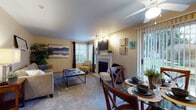 This single-floor residence is thoughtfully laid out to maximize both functionality and comfort. The living room serves as the heart of the home, featuring plush wall-to-wall carpeting, warm beige walls, and a classic white fireplace that anchors the space. A ceiling fan overhead and multiple windows allow ample natural light to fill the room, while track lighting adds supplemental illumination. The living area flows seamlessly into the dining space, which benefits from a sliding glass door that opens directly to a private outdoor patio, framing views of surrounding greenery.

The kitchen is efficiently designed with light wood cabinetry trimmed in warm tones, laminate countertops, and wood-look flooring. It includes a full suite of white appliances—refrigerator, electric range, dishwasher, and range hood—along with a pass-through window that connects to the dining area, enhancing the open feel.

The bedrooms are carpeted and finished in soft neutral tones, each offering windows with blinds for light control and privacy. The bathroom features a full tub-shower combination with clean white surrounds and wood-look flooring, maintaining the cohesive, understated aesthetic found throughout the entire residence.