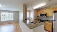 This single-floor residence offers a thoughtfully designed layout that balances open living spaces with comfortable private quarters. The living area is bright and spacious, featuring warm light hardwood flooring and a large window that fills the room with natural light and provides views of the surrounding exterior. A peninsula-style kitchen opens directly to the living space, anchored by granite countertops, light wood cabinetry, and stainless steel appliances including a gas range and over-the-range microwave. The kitchen also features tile flooring and ample counter and cabinet storage, with a window that brings in additional natural light. The bedrooms are generously sized, each finished with plush wall-to-wall carpeting and neutral warm-toned walls. One bedroom benefits from a private en-suite bathroom, while the additional full bathroom is outfitted with tile flooring, a granite-top vanity with wood cabinetry, and a full soaking tub with a tiled shower surround. Throughout the residence, a consistent neutral color palette and clean architectural lines create a calm, cohesive ambiance that is both functional and inviting.