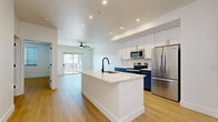 Located at 18220 N 68th St in Phoenix, AZ, this thoughtfully designed one-bedroom, one-bathroom residence offers a clean, modern aesthetic throughout its single-floor layout. Light-toned hardwood-style flooring flows seamlessly across every room, creating a cohesive and airy feel.

The open-concept kitchen and living area serves as the heart of the home. The kitchen is a standout, featuring a large central island with a white quartz countertop and matte black sink, upper white shaker cabinets with gold hardware, and contrasting navy blue lower cabinets. Stainless steel appliances, including a refrigerator, electric range, and microwave, complement the geometric tile backsplash. Recessed lighting illuminates the space, which flows naturally into the living room. The living area is bright and airy, with a ceiling fan, sliding glass doors, and access to a private balcony overlooking the surrounding community.

The bedroom is comfortably sized, featuring a ceiling fan, a window with natural light, and warm flooring. A dedicated closet provides organized storage. The bathroom includes a dark-cabineted vanity with gold hardware and a tiled surround. A separate laundry area with an in-unit washer and dryer adds everyday convenience. The hallway connects all spaces efficiently, completing this well-appointed residence.