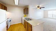 Located at 13731 Goldmark Dr in Dallas, TX, this single-floor, one-bedroom, one-bathroom unit offers a functional and cohesive layout. The kitchen is equipped with warm wood-toned cabinetry, light countertops, a double stainless steel sink, a white appliance suite including a refrigerator and electric range, and hardwood-style flooring. A breakfast bar peninsula connects the kitchen to the open living area, which is finished with plush carpeting and a ceiling fan with integrated lighting, creating a comfortable and unified common space. A window at the far end of the living area allows natural light to filter in. The bedroom is a well-proportioned room featuring soft carpet, a ceiling fan, and a large window with exterior views, filling the space with natural light. A dedicated closet provides practical storage. The bathroom includes a wood-toned vanity with a light stone-look countertop, a large mirror, hardwood-style flooring, and a tub/shower combination with white tile surround and accessibility grab bars. Neutral wall tones and consistent finishes throughout give the unit a clean, cohesive appearance. The layout, as visible in the dollhouse view, is efficiently organized with clear separation between living and sleeping areas.