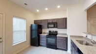 This single-floor apartment at Windhurst Park Apartments offers a practical and comfortable layout with thoughtfully designed interiors throughout. The kitchen is a standout feature, showcasing rich dark espresso cabinetry, granite-look countertops, and a full suite of black appliances including a refrigerator, electric range, and built-in microwave. Light wood-style flooring and recessed lighting complete the bright, functional cooking space, which also benefits from natural light through a window with blinds. The bedrooms are finished with plush wall-to-wall carpeting and neutral warm-toned walls, creating a cozy atmosphere. Each bedroom includes a ceiling fan with light fixture and windows fitted with blinds, allowing for both ventilation and natural light control. The bathrooms are clean and well-appointed, featuring dark vanity cabinetry with granite-look countertops, tile flooring, and a tub-shower combination. The primary bathroom includes a large vanity with an illuminated mirror. A dedicated laundry room provides added convenience, with washer and dryer hookups, wire shelving, and tile flooring. Throughout the apartment, consistent finishes and neutral tones create a cohesive and move-in-ready living environment.