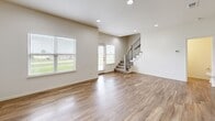 Located in Gardner, Kansas, this two-story home offers a well-designed layout across two floors, accommodating four bedrooms and three bathrooms. The main level features an open-concept kitchen and living area with warm wood-look luxury vinyl plank flooring, recessed lighting, and a large window that brings in natural light and views of the surrounding neighborhood. The kitchen is equipped with granite countertops, a central island with a sink, gray shaker-style cabinetry, and stainless steel appliances, creating a functional and stylish space for cooking and entertaining. The main floor also includes a dedicated hallway and convenient access to the attached garage, which features a wide concrete floor and an automatic opener. The laundry room is plumbed and ready for hookups. Upstairs, the primary bedroom is generously sized, featuring a tray ceiling, plush carpeting, and a large window with outdoor views. A spacious walk-in closet with wire shelving provides ample storage. Additional bedrooms offer vinyl plank flooring and natural light. The bathrooms include tile flooring and clean, neutral finishes. Outside, the home is framed by a well-maintained green lawn with a patio area, complementing the modern exterior with board-and-batten siding detailing.