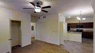 This single-floor space offers a practical and open layout designed for comfortable everyday living. The main living area features wall-to-wall carpeting that adds warmth underfoot, while a ceiling fan with a built-in light fixture provides both air circulation and ambient lighting overhead. The walls are finished in a neutral tone, creating a bright and clean backdrop throughout.

A prominent feature of the main room is the large double-door closet, offering generous storage capacity. Adjacent to the closet, a doorway leads into the kitchen, which transitions to tile flooring and is equipped with dark wood cabinetry and a light-toned countertop, providing a functional contrast to the living space. Recessed lighting in the kitchen adds a focused, practical illumination to the cooking area.

A second doorway from the main room provides additional access, suggesting a connected and efficiently organized floor plan. Vents are visible along the upper walls, indicating a central HVAC system for year-round climate control. The overall layout is straightforward and well-proportioned, making it easy to navigate and furnish. The neutral color palette and consistent finishes throughout give the space a cohesive and move-in-ready appearance.