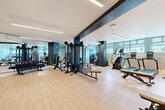 Located at 6 Rantoul Street in Beverly, MA, this fitness center offers a thoughtfully designed exercise space that provides a comprehensive workout environment. The room features light hardwood-style flooring, crisp white ceilings with sleek linear lighting, and bold navy accent beams and columns that lend a contemporary aesthetic throughout.

The space is organized into distinct functional zones. The cardio area is lined with Matrix treadmills, stair climbers, and stationary bikes, positioned along a windowed wall that allows natural light to filter in through roller-shaded windows, offering views of the surrounding area. The strength training zone features a multi-station cable machine system, a dumbbell rack with a full range of free weights, and adjustable benches. A dedicated functional fitness area provides open floor space alongside a rack stocked with medicine balls, kettlebells, and stability balls for dynamic workouts.

Full-length mirrors along one wall visually expand the space and support proper form during exercise. The room's light teal and white color palette, combined with neutral flooring and bold dark accents, creates an energizing yet focused atmosphere well-suited for a variety of fitness routines. The layout is open and efficiently organized, ensuring comfortable circulation between equipment zones.