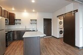 This single-floor unit offers a thoughtfully designed open-concept layout with a clean, modern aesthetic throughout. The kitchen serves as a central feature, equipped with stainless steel appliances including a refrigerator, range, microwave, and dishwasher. Rich dark cabinetry is complemented by light quartz-style countertops, open floating shelves, and a central island that provides additional workspace and storage. A glass backsplash adds a sleek finishing touch.

Warm hardwood-style flooring runs consistently throughout the entire unit, creating a cohesive and inviting atmosphere. The two bedrooms are generously sized, each featuring ceiling fans, large windows that invite natural light, and direct access to walk-in closets with built-in shelving. The open layout of each bedroom allows for flexible furniture arrangements.

The bathroom is well-appointed with a navy blue vanity, framed mirror, a soaking tub, and matching hardwood-style flooring that ties the space together. Exposed ductwork visible in the main living area introduces an industrial design element, adding character and contrast to the otherwise clean, neutral interior. Dark-framed interior doors and bold black baseboards provide sharp, modern detailing throughout the unit.