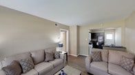 This single-story, 2-bedroom, 1.5-bathroom unit offers a practical and comfortable layout designed to maximize its well-utilized footprint. The living room serves as the central gathering space, featuring wood-style plank flooring, neutral warm-toned walls, and a large window that allows natural light to fill the room. The open sightline connects the living area to the kitchen, enhancing the sense of space throughout.

The kitchen is equipped with dark cabinetry providing ample storage, dark granite-style countertops, a double sink, and black appliances including an electric range, dishwasher, and refrigerator. Adjacent to the kitchen, a dedicated laundry area with a washer is also present.

Both bedrooms feature the same wood-style flooring, neutral walls, textured ceilings, and windows that bring in natural light. At least one bedroom includes a closet with built-in shelving. The full bathroom is outfitted with a tiled tub-shower combination and a curtain rod, while the half bathroom features a dark granite-topped vanity, a wall-mounted mirror, and an overhead light fixture. The overall aesthetic throughout is clean, neutral, and functional.