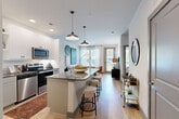 Located at 235 Verbena St in Charlotte, NC, this well-appointed one-bedroom, one-bathroom residence offers a thoughtfully designed single-floor layout. The open-concept living and kitchen area forms the heart of the home, where white shaker cabinetry, subway tile backsplash, stainless steel appliances, and a central island with seating create a functional and stylish kitchen. Recessed lighting and pendant fixtures illuminate the space, while light hardwood-style flooring flows throughout. The living room receives generous natural light through large windows and a glass door that opens to a private outdoor balcony, providing views of the surrounding greenery. The bedroom offers a comfortable retreat with ample natural light from dual windows, a ceiling fan, and direct access to the walk-in closet. The bathroom features a full tub-shower combination with large-format white tile, wood-look flooring, and rustic floating shelves for storage. A dedicated closet with built-in shelving and a separate laundry area and utility room round out the practical amenities. The overall design balances modern finishes with a warm, inviting ambiance throughout.