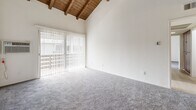 Located at 1560 S Highland Ave in Fullerton, CA, this two-bedroom, two-bathroom residence offers a thoughtfully designed single-floor layout with a range of comfortable living spaces. The living room immediately impresses with soaring vaulted ceilings adorned with exposed wooden beams and tongue-and-groove wood paneling, creating a warm, architectural focal point. Sliding glass doors connect the living area to a private balcony, inviting natural light and outdoor views into the space. Soft carpeting runs throughout the living and bedroom areas, while light-toned luxury vinyl plank flooring extends through the kitchen, hallways, and bathrooms. The kitchen is equipped with warm wood cabinetry, granite-style countertops, a full suite of appliances including a stove, microwave, and refrigerator, and is finished with recessed lighting and a ceiling fan overhead. A pantry provides additional storage convenient to the kitchen. The primary bedroom offers generous proportions, a walk-in closet, and an en-suite bathroom featuring a wood vanity with stone countertop. The second bedroom is bright and well-sized, with a large window and closet. The second bathroom mirrors the same clean, functional design with a tub-shower combo and matching wood vanity. With four closets total and a dedicated hallway, storage and flow are well-considered throughout.