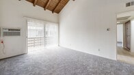 Located at 1560 S Highland Ave in Fullerton, CA, this two-bedroom, two-bathroom residence offers a thoughtfully designed single-floor layout with a range of comfortable living spaces. The living room immediately impresses with soaring vaulted ceilings adorned with exposed wooden beams and tongue-and-groove wood paneling, creating a warm, architectural focal point. Sliding glass doors connect the living area to a private balcony, inviting natural light and outdoor views into the space. Soft carpeting runs throughout the living and bedroom areas, while light-toned luxury vinyl plank flooring extends through the kitchen, hallways, and bathrooms. The kitchen is equipped with warm wood cabinetry, granite-style countertops, a full suite of appliances including a stove, microwave, and refrigerator, and is finished with recessed lighting and a ceiling fan overhead. A pantry provides additional storage convenient to the kitchen. The primary bedroom offers generous proportions, a walk-in closet, and an en-suite bathroom featuring a wood vanity with stone countertop. The second bedroom is bright and well-sized, with a large window and closet. The second bathroom mirrors the same clean, functional design with a tub-shower combo and matching wood vanity. With four closets total and a dedicated hallway, storage and flow are well-considered throughout.