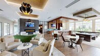 Located at 1000 Antietam Creek Dr in Fayetteville, NC, this well-appointed community amenity center offers a comprehensive suite of shared spaces designed for comfort, productivity, and entertainment. The single-floor layout spans a generous footprint, thoughtfully organized into distinct functional areas.

The central lounge area serves as the heart of the facility, featuring warm hardwood-style flooring, a sleek linear fireplace set against a dramatic dark tile accent wall, and a striking sculptural chandelier overhead. Plush neutral seating arrangements and a green curved accent piece add contemporary flair, while a wet bar and kitchenette with rich wood cabinetry, a teal glass backsplash, and stainless steel appliances provide convenient refreshment options.

Adjacent to the lounge, a dedicated theater room impresses with reclining leather seats, cup holders, a large projection screen, and a starfield ceiling, creating an immersive cinematic experience. A glass-walled conference room floods with natural light and outdoor views, accommodating group meetings with a full complement of modern seating. The business center features workstations, vibrant red chairs, and floor-to-ceiling windows that invite the outdoors in. Completing the amenities, a well-equipped laundry facility offers multiple stacked washer and dryer units with direct exterior access and natural light.