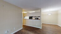 This single-floor residence offers a well-organized, open-concept layout designed for comfortable everyday living. The main living area is finished with rich, dark hardwood-style flooring and features a large sliding glass door dressed with vertical blinds, allowing natural light to fill the space and providing outdoor access. A pendant light fixture adds a finishing touch to the adjacent dining area.

The kitchen is positioned behind a half-wall pass-through counter, creating a connected yet defined cooking space. Inside, dark espresso cabinetry lines both walls, offering generous storage, while stone-look countertops provide ample prep space. Black appliances, including a refrigerator, electric range, and overhead microwave, complete the functional kitchen setup. The hardwood-style flooring continues seamlessly throughout.

The bedroom is a quiet, carpeted retreat with a window that invites natural light and provides a warm, restful ambiance. The textured ceilings carry consistently throughout the home, adding a classic residential character.

The bathroom is clean and straightforward, featuring a full-size soaking tub and shower combination with chrome fixtures. Throughout the home, neutral warm-toned walls, white trim, and consistent finishes create a cohesive and inviting atmosphere.