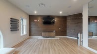 Located at 200 W Main St in New Albany, Ohio, this single-floor commercial space offers a clean, modern interior designed for both function and style. The main area is immediately distinguished by its striking dark wood plank accent walls, which span the full width of the room and lend a warm, contemporary character to the space. These wood-paneled walls serve as a natural focal point, enhanced further by a wall-mounted flat-screen display and a sleek low-profile media credenza positioned beneath it — making the space well-suited for presentations, meetings, or events.

The light-toned hardwood flooring runs throughout, complementing the wood accent walls while keeping the overall aesthetic bright and inviting. Recessed ceiling lighting provides even, ambient illumination across the room, and in-ceiling speakers suggest integrated audio capabilities. A window along one wall allows natural light to filter into the space, adding to its open and airy feel.

The layout is notably open and flexible, with generous floor area that can be configured to accommodate a variety of uses. The combination of polished finishes, thoughtful built-in technology, and versatile open floor plan makes this a well-appointed space suitable for professional, hospitality, or community-oriented purposes.