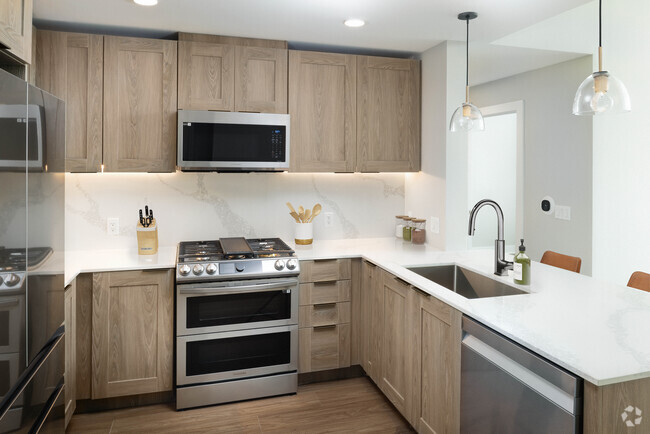 Signature Collection kitchen with stainless steel appliances, marbled white quartz countertops, brown cabinetry, and hard surface vinyl plank flooring (Representative photo) - Avalon W Squared