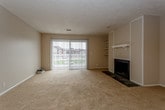 This single-floor residence offers a functional and comfortable layout designed to maximize living space. The expansive living area is highlighted by plush wall-to-wall carpeting and a classic wood-mantel fireplace, creating a warm and inviting focal point. Large sliding glass doors with vertical blinds allow natural light to fill the room while providing access to the outdoors. A ceiling fan adds to the comfort of the space.

The galley-style kitchen is efficiently laid out with ample white cabinetry on both sides, dark countertops, a double-basin sink, and black appliances including a range and dishwasher, alongside a full-size refrigerator. Light vinyl tile flooring completes the kitchen's clean, practical aesthetic.

The bedrooms are generously sized, each featuring soft carpeting and windows with blinds that bring in natural light. Textured ceilings are consistent throughout the home, adding subtle architectural character.

The full bathroom is well-appointed with a tub-shower combination, a white vanity with under-cabinet storage, a large mirror, and tile accents along the walls. Light tile flooring ties the space together neatly.

Overall, this residence presents a straightforward, move-in-ready layout with neutral tones throughout, offering a versatile and comfortable living environment.