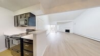 This 810 sq ft single-floor unit offers 2 bedrooms and 2 bathrooms. The bright living room features vaulted ceilings, light hardwood flooring, a wood-burning fireplace with a tile surround, and sliding glass doors providing outdoor access. The galley-style kitchen is equipped with dark cabinetry, white quartz countertops, black appliances, and a peninsula breakfast bar. Both bedrooms feature plush carpet, natural light, baseboard heating, and louvered sliding closet doors. The bathrooms include dark vanities, white quartz countertops, and tiled tub-shower combos with hardwood-style flooring throughout.