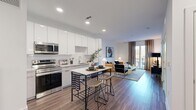 Located at Modera in Pine Brook, New Jersey, this one-bedroom, two-bathroom residence offers a thoughtfully designed, single-floor layout with contemporary finishes throughout. The open-concept kitchen and living area forms the heart of the home, anchored by a sleek kitchen equipped with stainless steel appliances—including a range, microwave, and dishwasher—glossy white upper cabinets, light wood-tone lower cabinets, a tile backsplash, and light quartz countertops. Wood-look plank flooring extends through the main living area, complementing the clean, modern aesthetic. The living room receives abundant natural light through floor-to-ceiling sliding glass doors that open onto a private balcony, offering outdoor views. The spacious primary bedroom features plush carpeting, a large window with ample natural light, and direct access to a dedicated walk-in closet. Two well-appointed bathrooms serve the residence; the primary bath includes a dual-sink vanity with a backlit mirror and wood-tone cabinetry, while the second bath features a full tub-shower combination with crisp white subway tile surround. Recessed lighting throughout maintains a bright, polished ambiance across the entire residence.