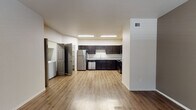 This single-floor residence offers a clean, modern design highlighted by warm wood-look flooring that flows consistently throughout every room, creating a cohesive and inviting atmosphere. The open-concept kitchen serves as the centerpiece of the unit, showcasing rich dark espresso cabinetry, granite-style countertops, and a full suite of stainless steel appliances including a refrigerator, dishwasher, range, and microwave. Recessed skylight-style ceiling panels provide bright, even illumination over the kitchen workspace, while an adjacent walk-in pantry offers generous storage. The living area is spacious and open, benefiting from natural light through blinds-covered windows and a direct view into the kitchen, ideal for everyday living. The bedroom features a ceiling fan, two windows that invite natural light, and a clean, neutral palette that offers flexibility for any décor style. The bathroom continues the design language of the kitchen with matching dark cabinetry, granite-topped vanity, and a large mirror. A dedicated in-unit laundry area with a washer and dryer adds everyday convenience. Neutral walls and consistent finishes throughout give this residence a fresh, move-in-ready character.