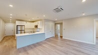 This single-floor unit showcases a clean, modern design highlighted by light hardwood flooring that runs consistently throughout the space. A long, well-lit corridor with recessed lighting leads from the entrance into the heart of the unit, where an open-concept kitchen and living area take center stage.

The kitchen is a standout feature, equipped with flat-front white cabinetry, a large waterfall-edge quartz island with an undermount sink and contemporary arc faucet, stainless steel appliances including a refrigerator, range, and built-in microwave, and sleek pendant lighting overhead. A ceiling-mounted HVAC cassette serves the adjoining living area, which opens directly to a private balcony through large glass doors, offering outdoor views.

The bedrooms are bright and airy, benefiting from multiple windows that bring in generous natural light and exterior views. The unit includes two bathrooms: one featuring large-format dark tile surrounding a soaking tub and shower combination, and a second with a glass-enclosed walk-in shower, dark tile surround, a floating vanity, and light marble-style floor tile. A louvred closet provides additional storage within the living area. Recessed lighting and clean white walls maintain a consistently fresh, contemporary ambiance throughout.