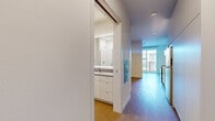 Located at 21 Boston St in Seattle's Queen Anne neighborhood, this efficient single-floor unit offers a thoughtfully designed layout that maximizes every square foot. The interior features warm wood-tone flooring throughout, crisp white walls, and a clean modern aesthetic that creates a bright, cohesive feel.

The kitchen is a standout feature, outfitted with full stainless steel appliances including a gas range, dishwasher, and refrigerator. Sleek white cabinetry extends floor to ceiling, providing ample storage, while a textured penny-tile backsplash adds a subtle design detail beneath under-cabinet lighting.

The living area benefits from a large sliding glass door that opens to a private balcony, inviting abundant natural light and offering open views of the surrounding Seattle cityscape — a particularly appealing feature given the elevated vantage point.

The bathroom is generously proportioned for the overall footprint of the unit, featuring a wide white vanity with an illuminated mirror, a walk-in tiled shower, and a stacked Whirlpool washer and dryer — a practical convenience integrated directly into the space.

Clean lines, recessed lighting, and a neutral palette throughout give the unit a modern, move-in-ready character well-suited to urban living in Seattle.