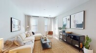 This single-floor residence is thoughtfully designed with a contemporary aesthetic, combining neutral tones, natural textures, and modern finishes throughout. The living area serves as the heart of the space, featuring light-washed walls, light wood-style flooring, and multiple windows dressed with linen curtains that invite abundant natural light. A sectional sofa anchors the room atop a woven jute rug, complemented by a sleek matte-black media console and curated wall art, creating a relaxed yet refined atmosphere.

The kitchen is a standout feature, showcasing two-toned cabinetry—sage green lower cabinets paired with crisp white uppers—alongside stainless steel appliances, subway tile backsplash, and a generous peninsula with a white quartz countertop. Pendant lighting above the peninsula adds a modern touch, while seating along the bar overhang makes it ideal for casual dining.

The bedroom is carpeted for comfort, featuring a large window that fills the room with natural light and direct access to a spacious walk-in closet. The full bathroom offers a clean, contemporary design with a wide vanity, white quartz countertop, wood-look flooring, and a full soaking tub with shower.